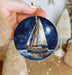 a hand holding a christmas ornament with a sailboat on it