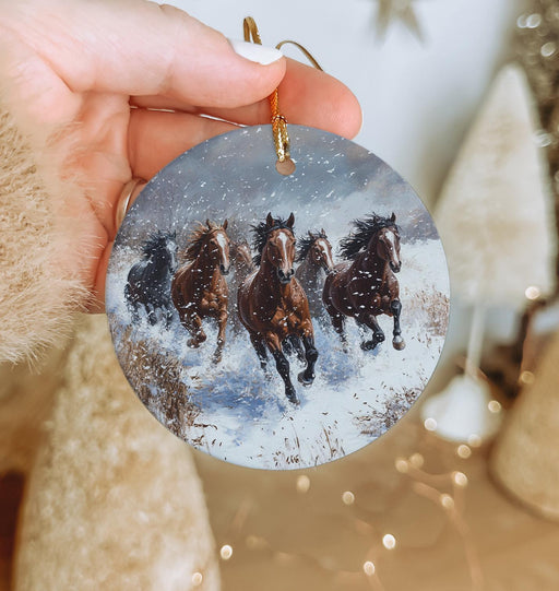 a hand holding a christmas ornament with horses running in the snow