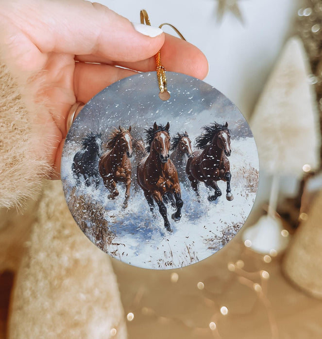 a hand holding a christmas ornament with horses running in the snow