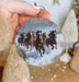 a hand holding a christmas ornament with horses running in the snow