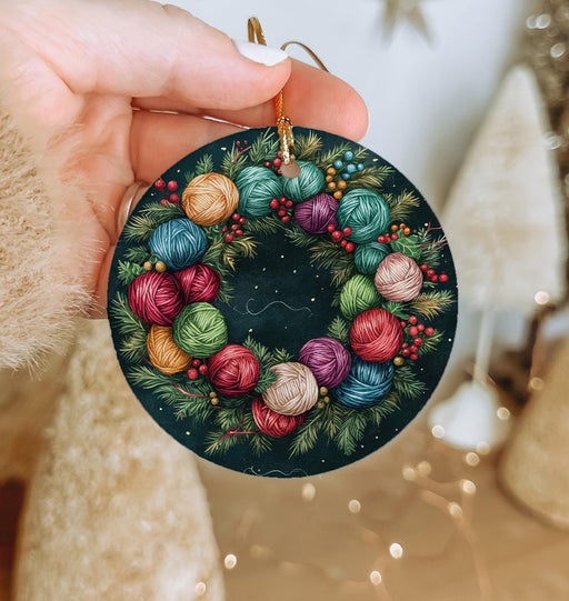 a hand holding a christmas ornament decorated with balls of yarn