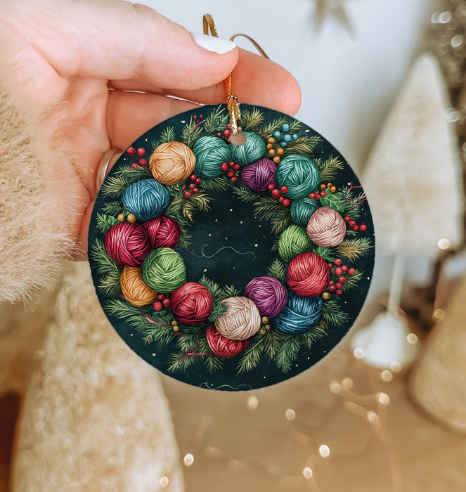a hand holding a christmas ornament decorated with balls of yarn