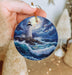 a hand holding a christmas ornament with a lighthouse on it