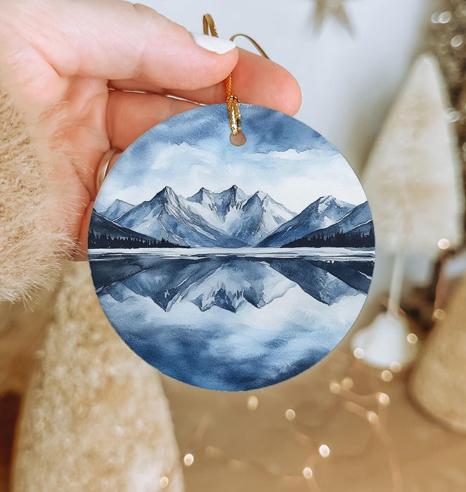 a hand holding a round ornament with a mountain scene on it