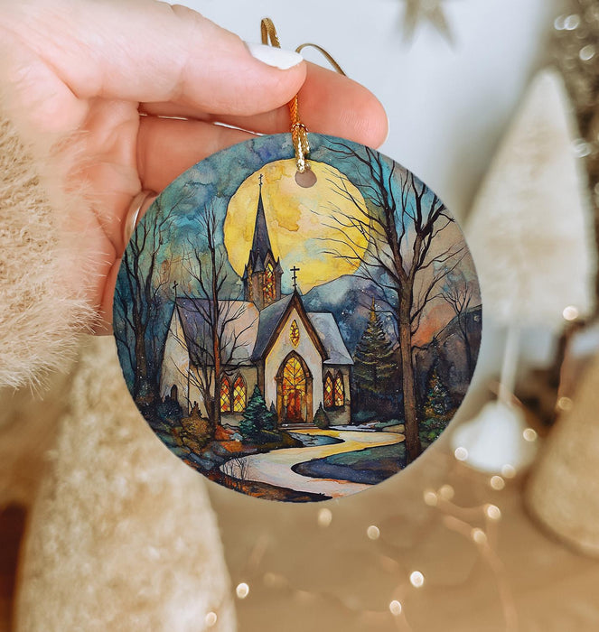 a hand holding a christmas ornament with a painting of a church