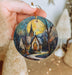 a hand holding a christmas ornament with a painting of a church