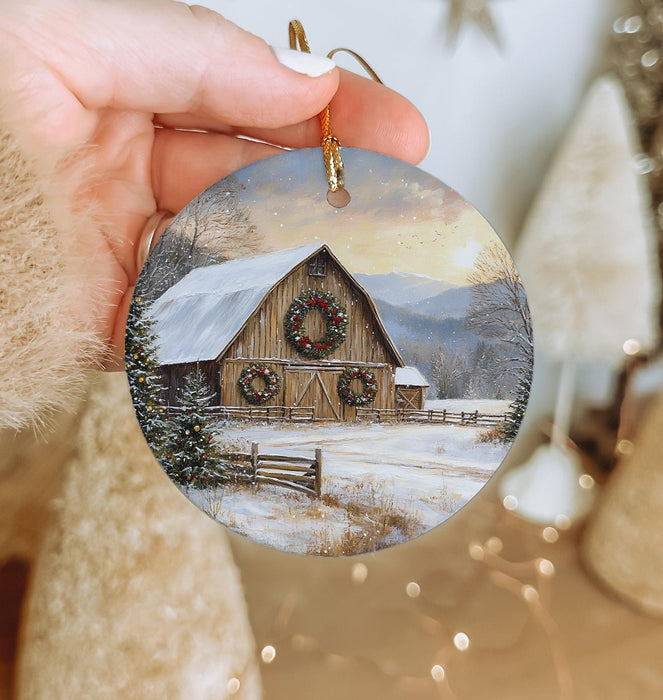 a person holding a christmas ornament with a barn in the background