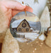 a person holding a christmas ornament with a barn in the background