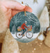 a hand holding a christmas ornament with a man riding a bike