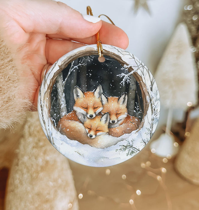 a hand holding a christmas ornament with two foxes