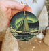 a person holding a christmas ornament with a sailboat on it
