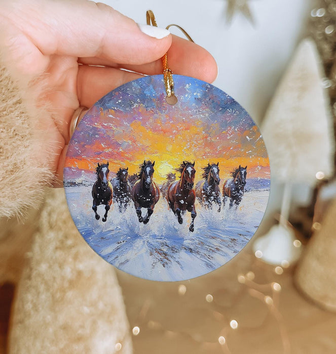 a hand holding a christmas ornament with horses running in the snow