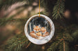 a glass ornament with two foxes hanging from a tree