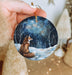 a hand holding a christmas ornament with a fox on it