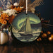 a christmas ornament with a sailboat in the ocean