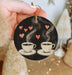 a hand holding a christmas ornament with two cups of coffee
