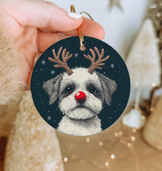 a hand holding a christmas ornament with a dog wearing reindeer antlers