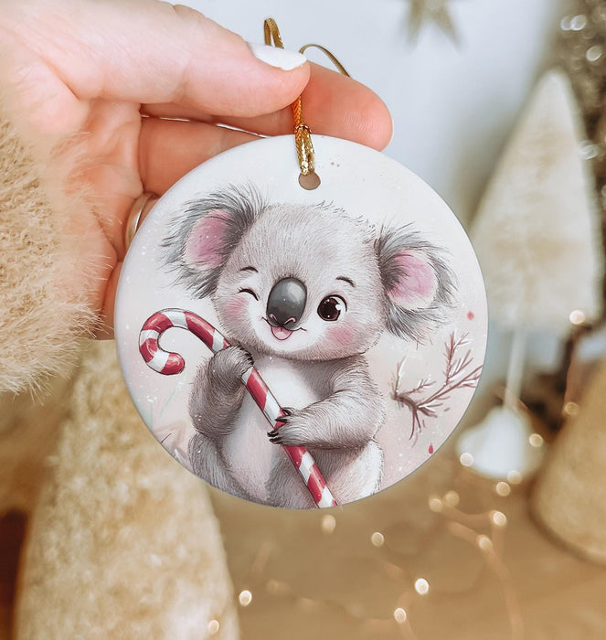 a hand holding a christmas ornament with a koala holding a candy cane