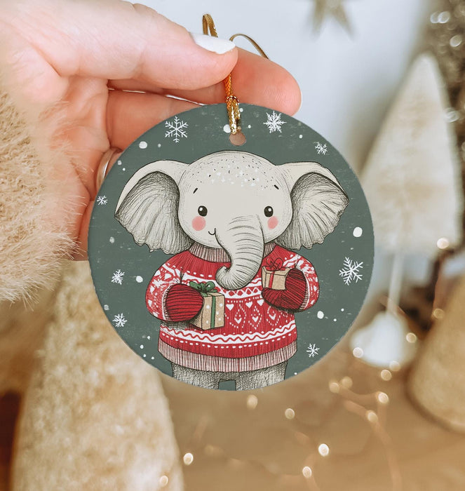a hand holding a christmas ornament with an elephant wearing a sweater