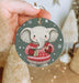 a hand holding a christmas ornament with an elephant wearing a sweater