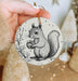 a hand holding a christmas ornament with a squirrel on it