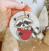a hand holding a christmas ornament with a raccoon