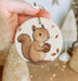 a hand holding a christmas ornament with a squirrel on it