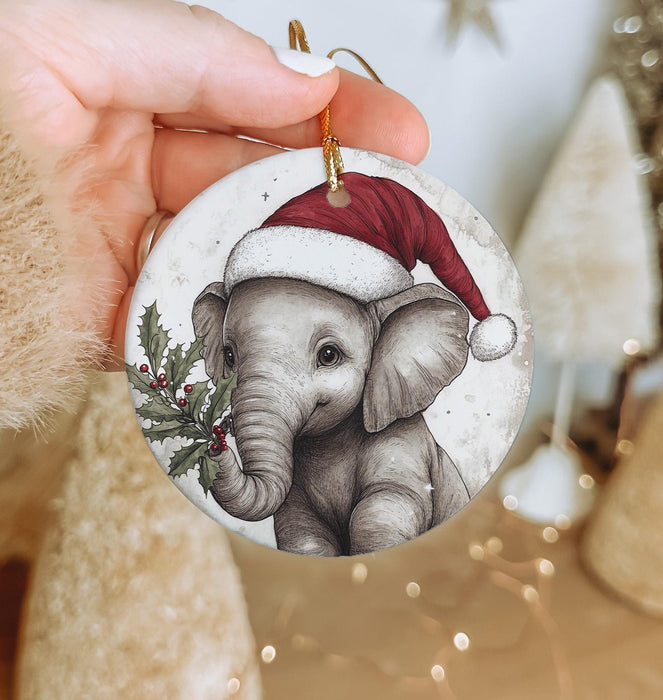 a hand holding a christmas ornament with an elephant wearing a santa hat