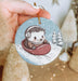 a hand holding a christmas ornament with a hedge riding a sleigh