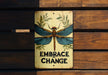 a sign that says embrace change with a dragonfly on it