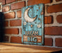 a wooden sign that says dream big on a brick wall