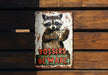 a metal sign with a raccoon holding a cup