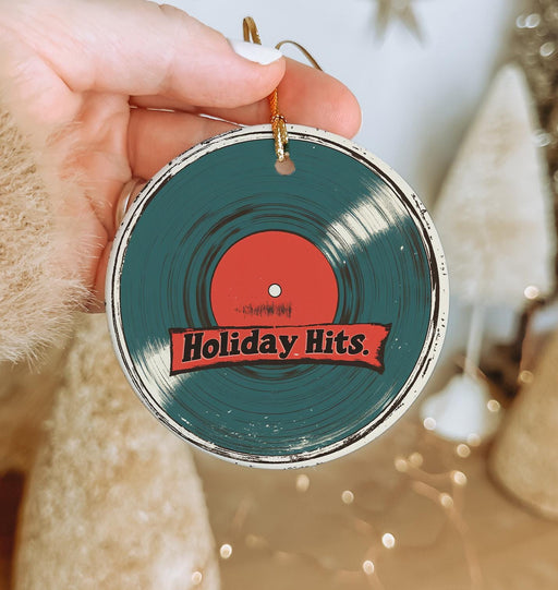 a person holding a christmas ornament with the word holiday hits on it