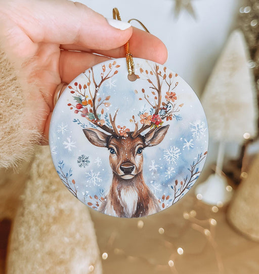 a hand holding a christmas ornament with a deer on it