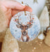 a hand holding a christmas ornament with a deer on it