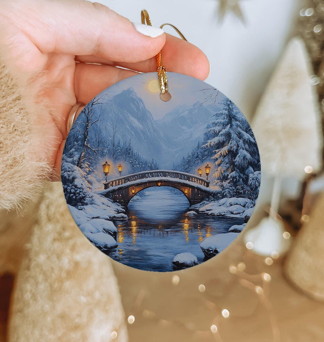 a person holding a christmas ornament with a bridge in the background