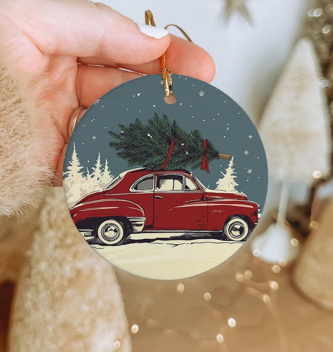 a hand holding a christmas ornament with a red car with a tree on