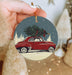 a hand holding a christmas ornament with a red car with a tree on