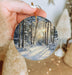 a person holding a christmas ornament with a snowy scene on it