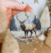 a hand holding a christmas ornament with a picture of a deer