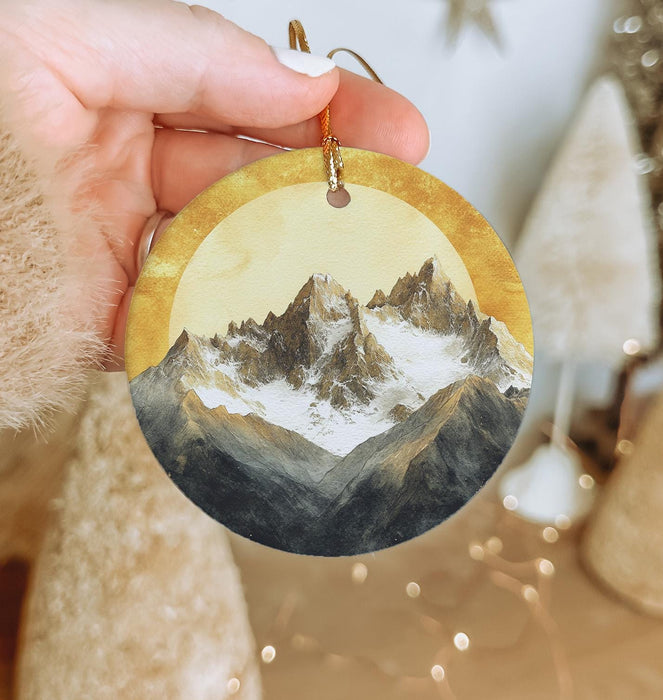 a hand holding a round ornament with a mountain scene on it
