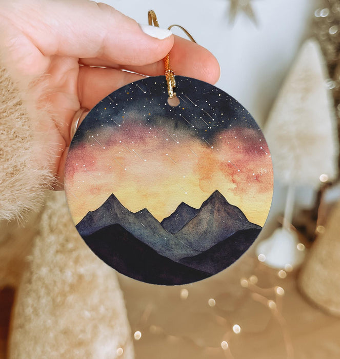a hand holding a round ornament with a painting of mountains