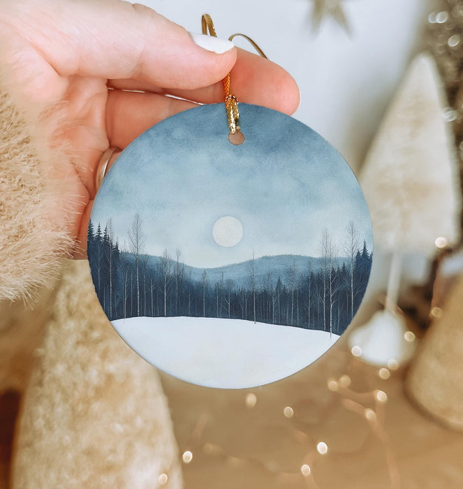 a hand holding a round ornament with a landscape painted on it