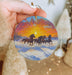 a hand holding a christmas ornament with horses running in the snow