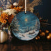 a christmas ornament with a painting of a snowy landscape