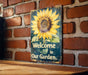 a sign that says welcome to our garden on a brick wall