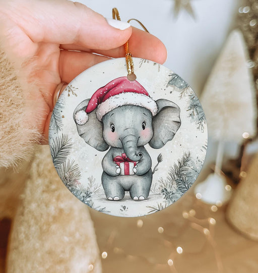 a hand holding a christmas ornament with an elephant wearing a santa hat