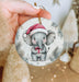 a hand holding a christmas ornament with an elephant wearing a santa hat