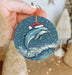 a hand holding a christmas ornament with a dolphin on it