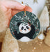 a hand holding a christmas ornament with a panda on it